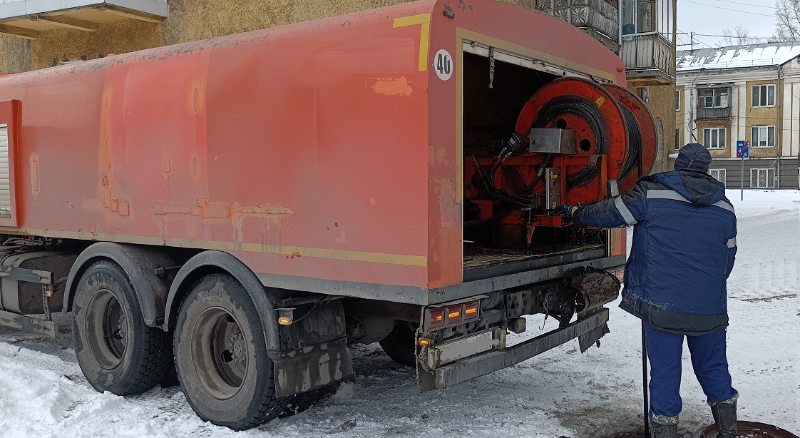 Каналопромывочная машина и работник прочищают засор в канализационной системе в Кривошеино